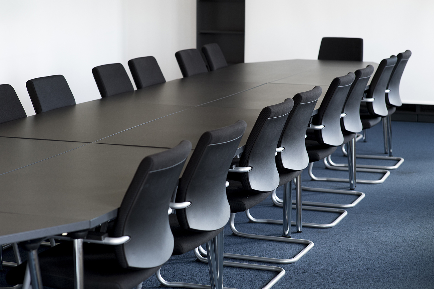 An image of a conference table and black chairs around it in a meeting room