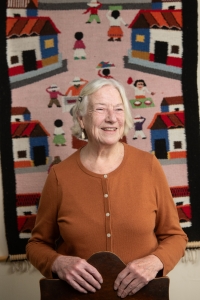 Woman in front of tapestry.