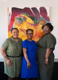 Three women of color in front of a colorful picture.