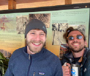 Two men pose outside in front of a national park sign