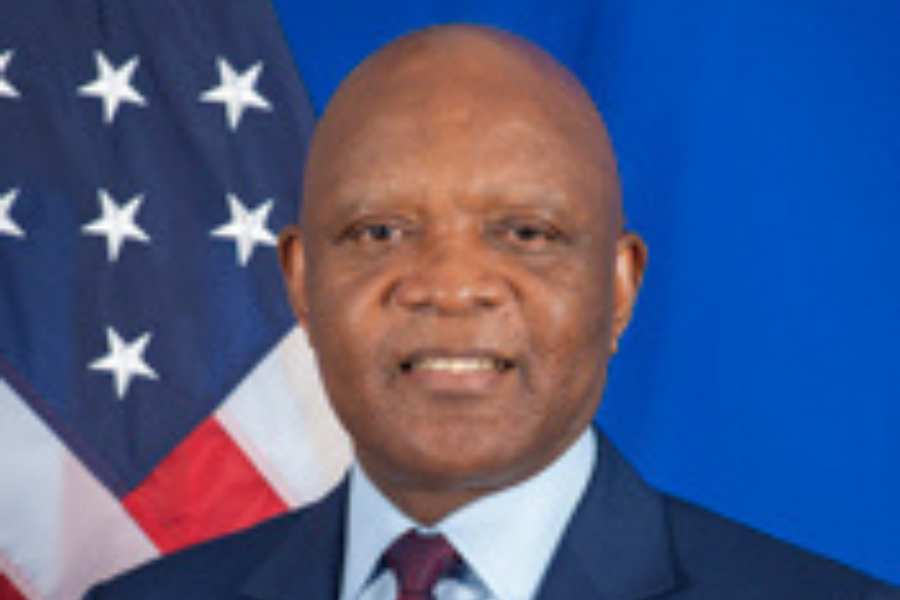 A headshot of a man in a suit in front of a U.S. flag