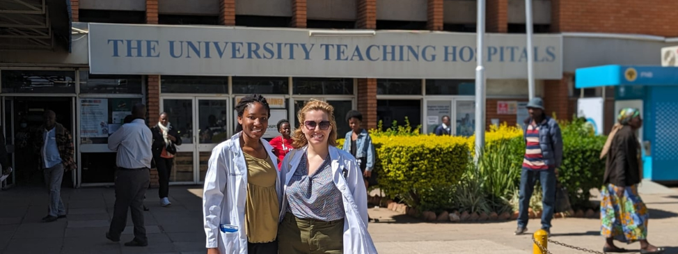 Two women in medical jackets stand outside a hospital in Zambia