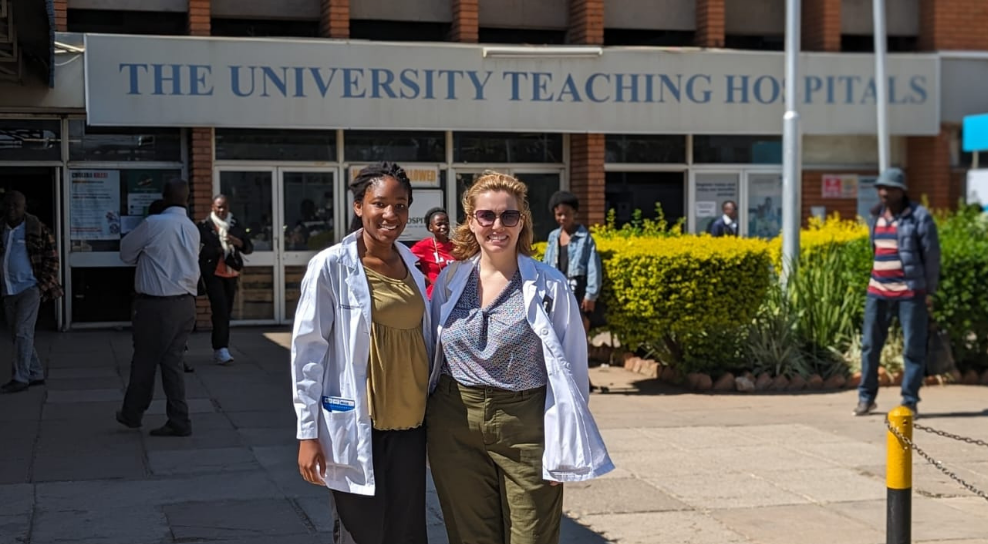 Two women in medical jackets stand outside a hospital in Zambia