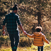 A father holding young son's hand as they walk in the woods