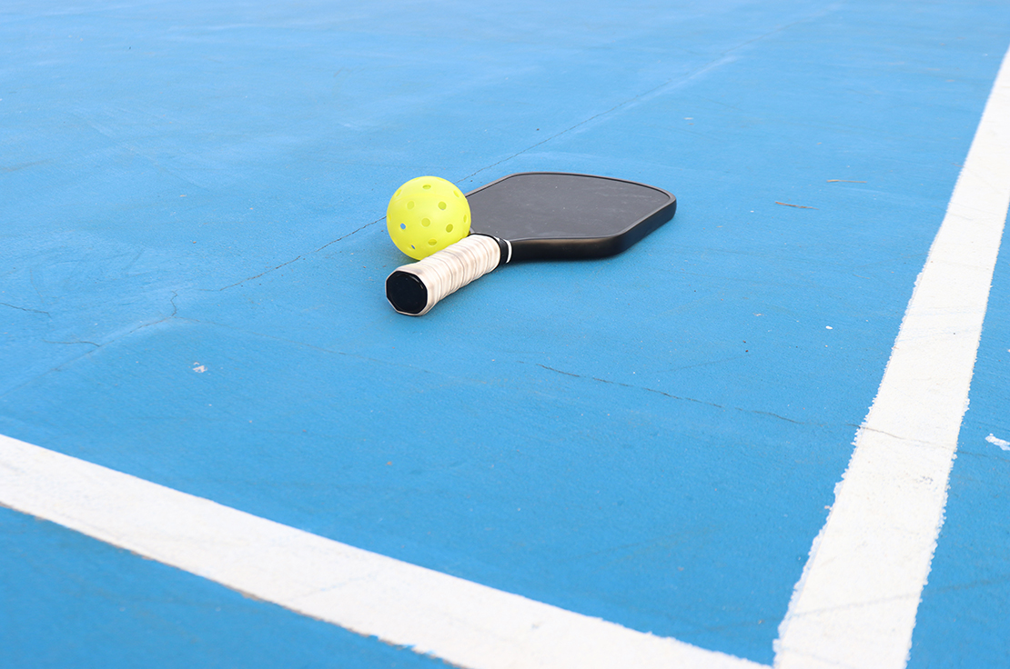 A pickleball paddle with a ball on the court.