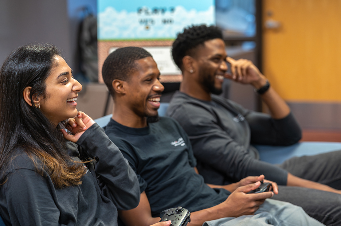 Three URecFit and Wellness students sitting on a couch smiling at a television